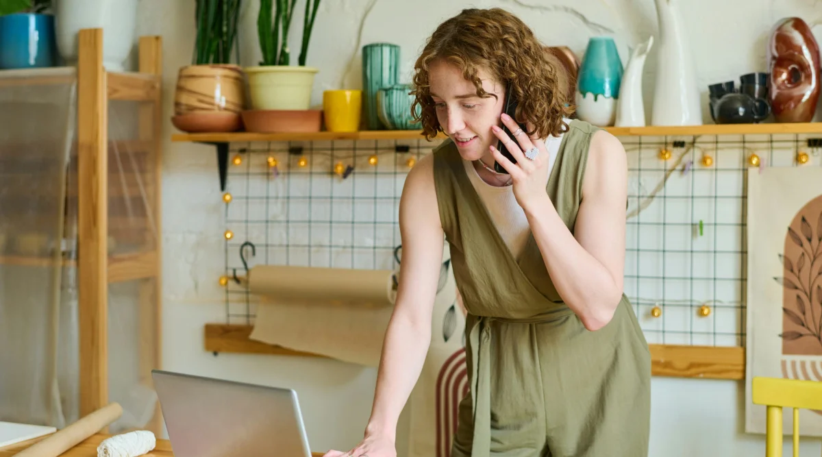 A woman talking on the phone while looking at her laptop.
