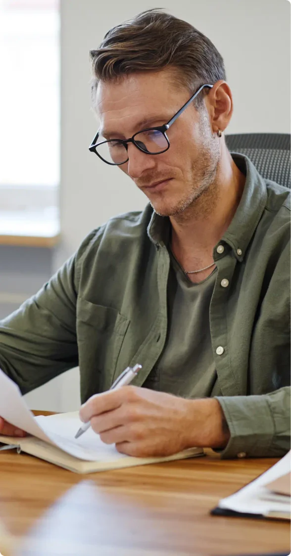 Brunette White man with a 5 o'clock shadow and glasses wearing a green button up shirt on top of green t-shirt filling out the dissolution paperwork that he received from LegalZoom.