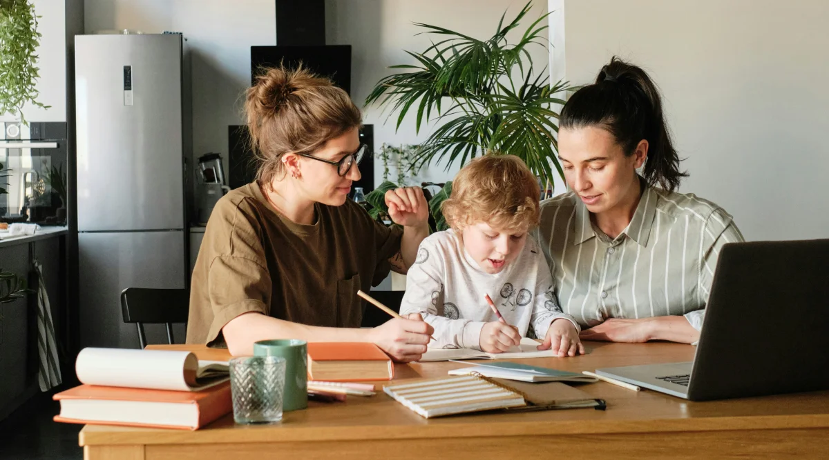 Two adult partners with a minor kid helping the child with his studies.