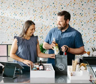 A man and a woman selecting wines for a gift bag.