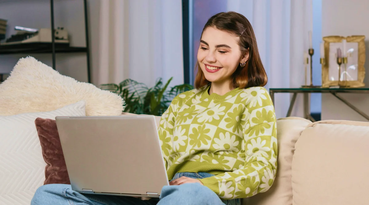 Woman in green sweater smiling while using a laptop