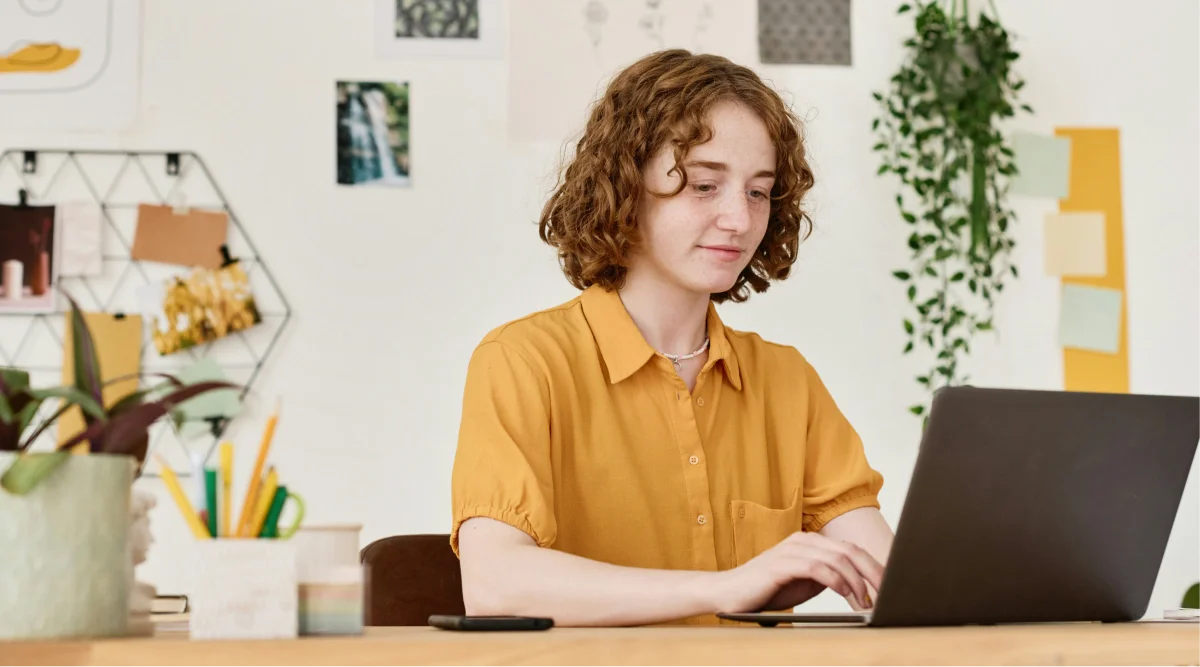 Person in yellow shirt working on a laptop at a desk