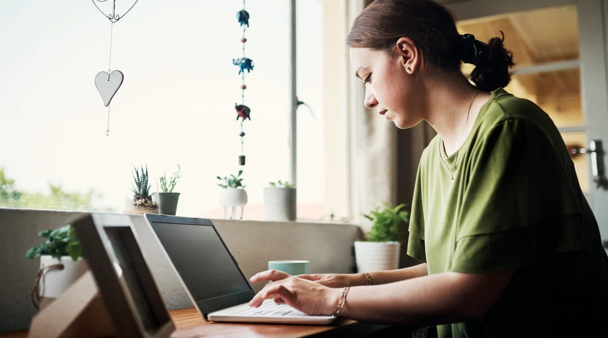 Woman in green shirt typing on a laptop by a window