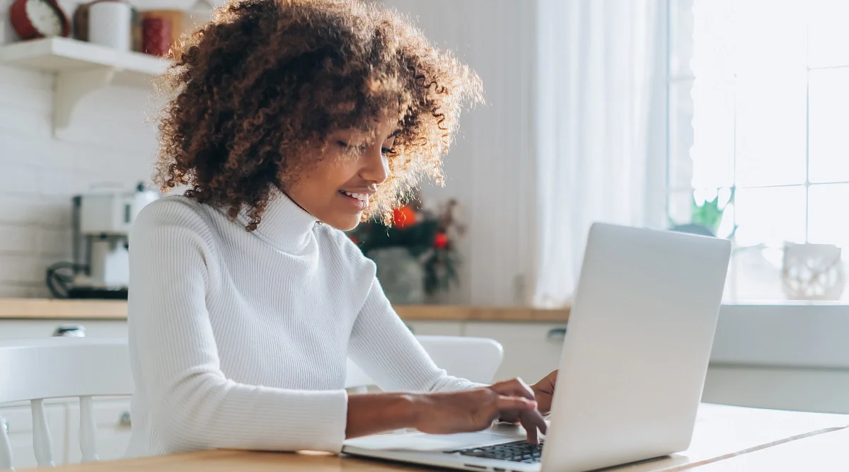 Smiling woman in white turtleneck using a laptop at home