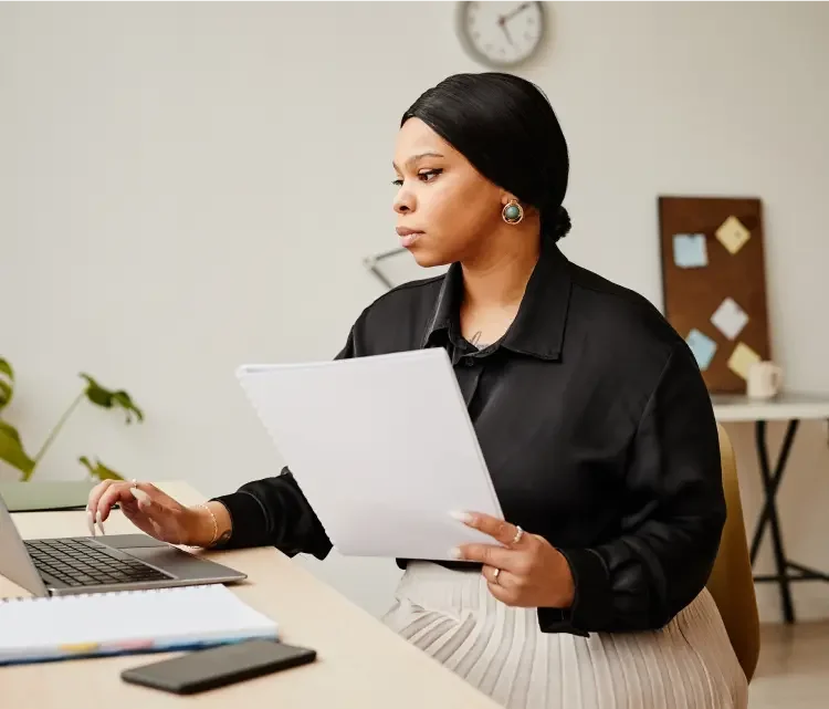 Black woman with her hair pulled back into a bun wearing a black blouse sitting in her office filling out her dissolution paperwork with LegalZoom.