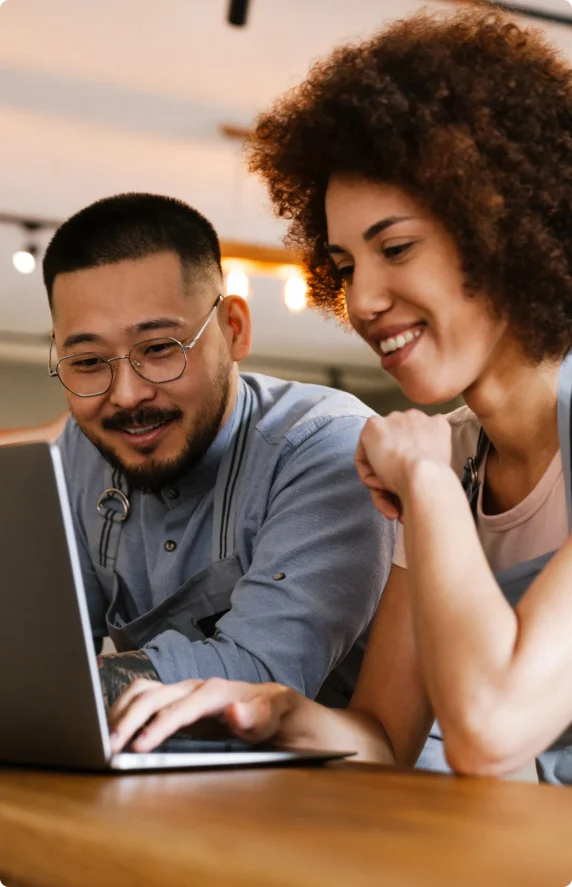 A man wearing glasses and a woman wearing an apron looking at a laptop.