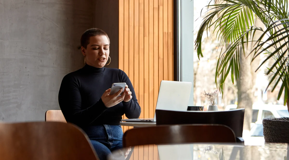 Woman using a phone in a cafe with a laptop