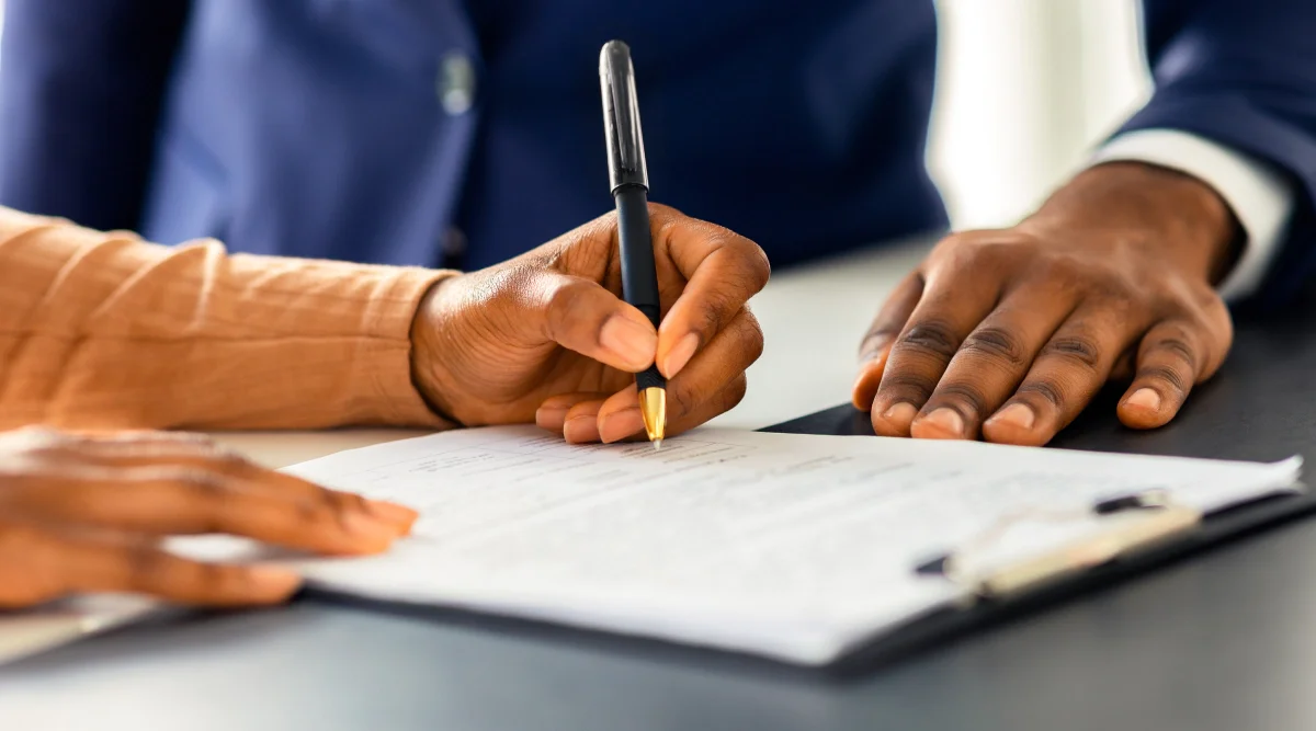 Close-up of hands signing a document on a clipboard