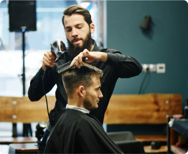 a hair stylist uses a blow dryer and brush for his client in a barber shop.