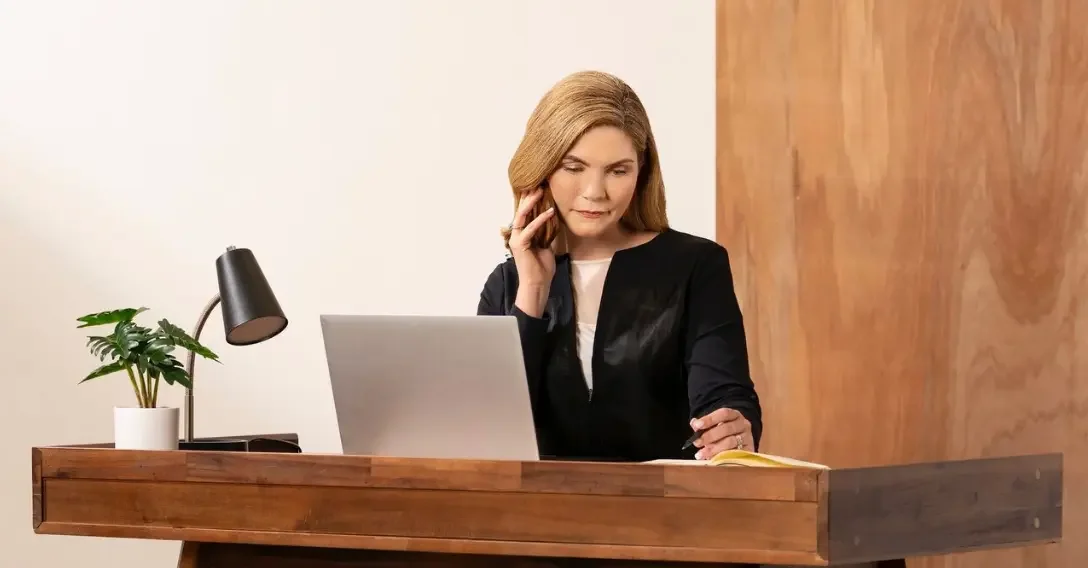 A blonde woman named Anne sitting at her desk talking on the phone with a client