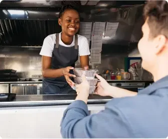 a young woman works the counter of a food truck and hands an order to a customer.