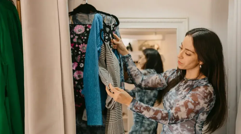 A woman stands in her closet going through her tops.