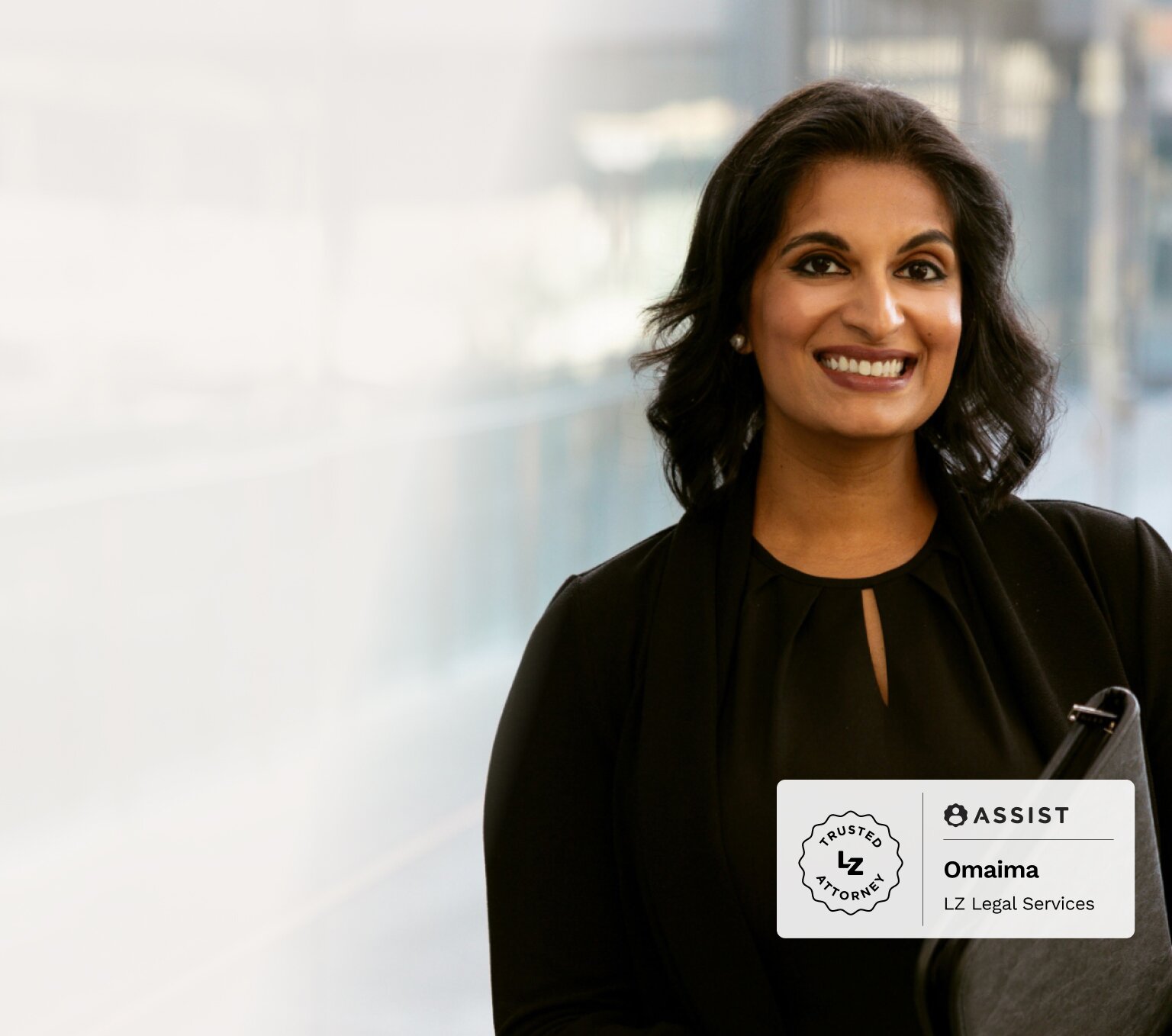 Woman wearing a black business suit smiles while holding her laptop