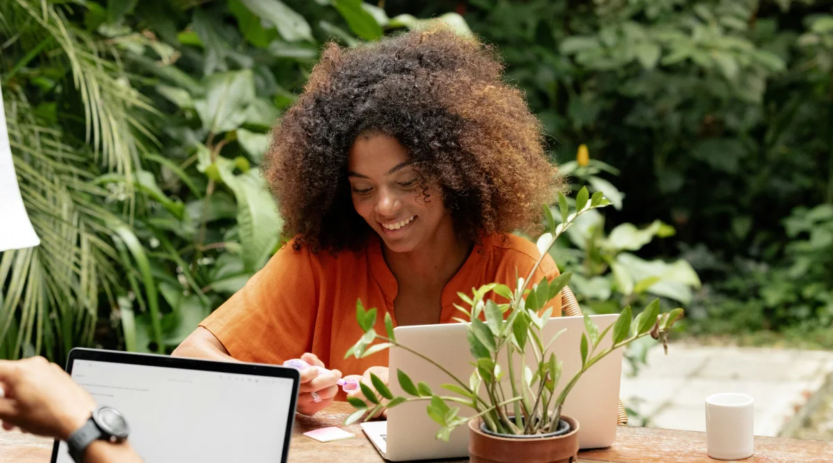 Woman working on a laptop outdoors surrounded by plants