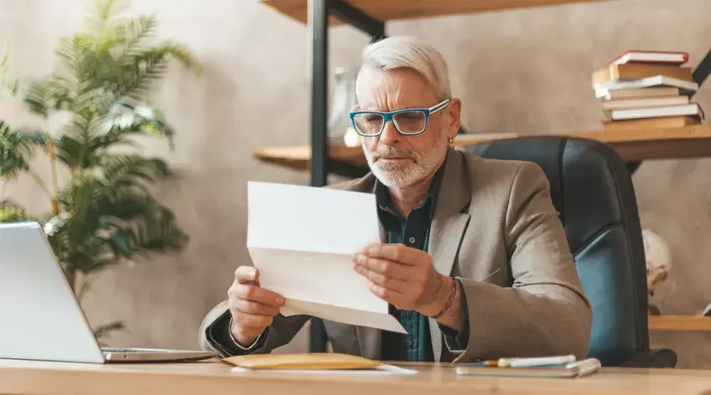 An elderly man sitting in his office tries to comprehend what made his father's will invalid as he reads a notice from the probate court.