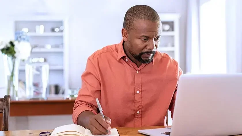 An image of a man reading on the laptop and making notes.