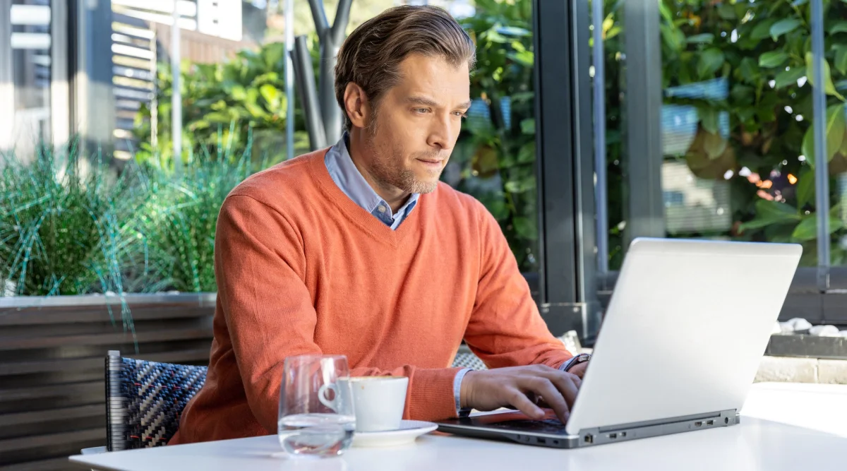 Man in orange sweater typing on a laptop outdoors