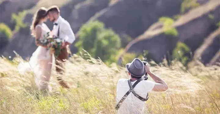A bride and groom stand in a field getting photographed.