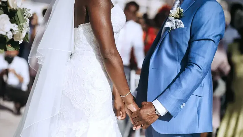 Close up of the midsections of a bride and groom facing each other and holding hands.