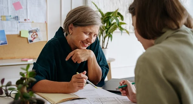 Two women smiling and reviewing paperwork together at a desk, symbolizing guidance and clarity in property deed services.