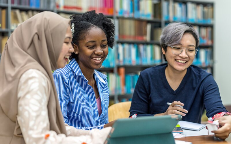 An image of 3 students in a library working on a project.