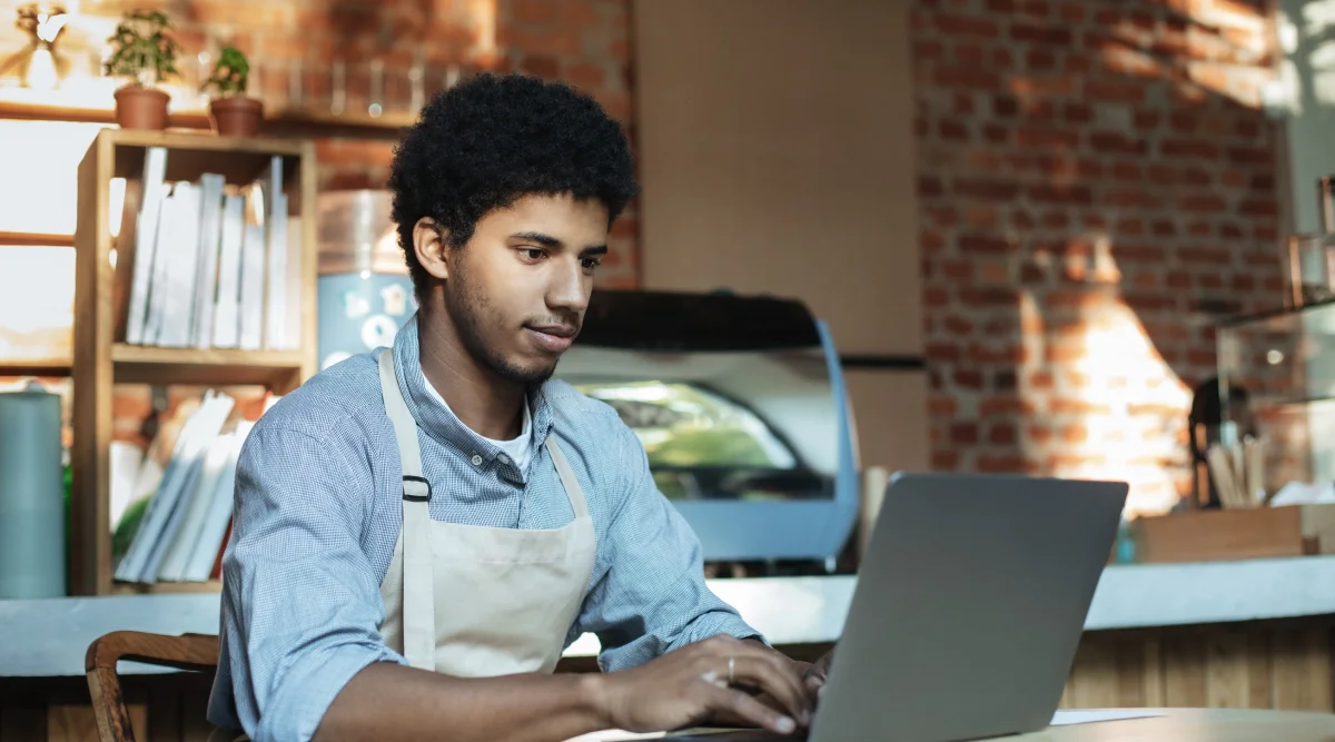 Man in apron using laptop in cafe