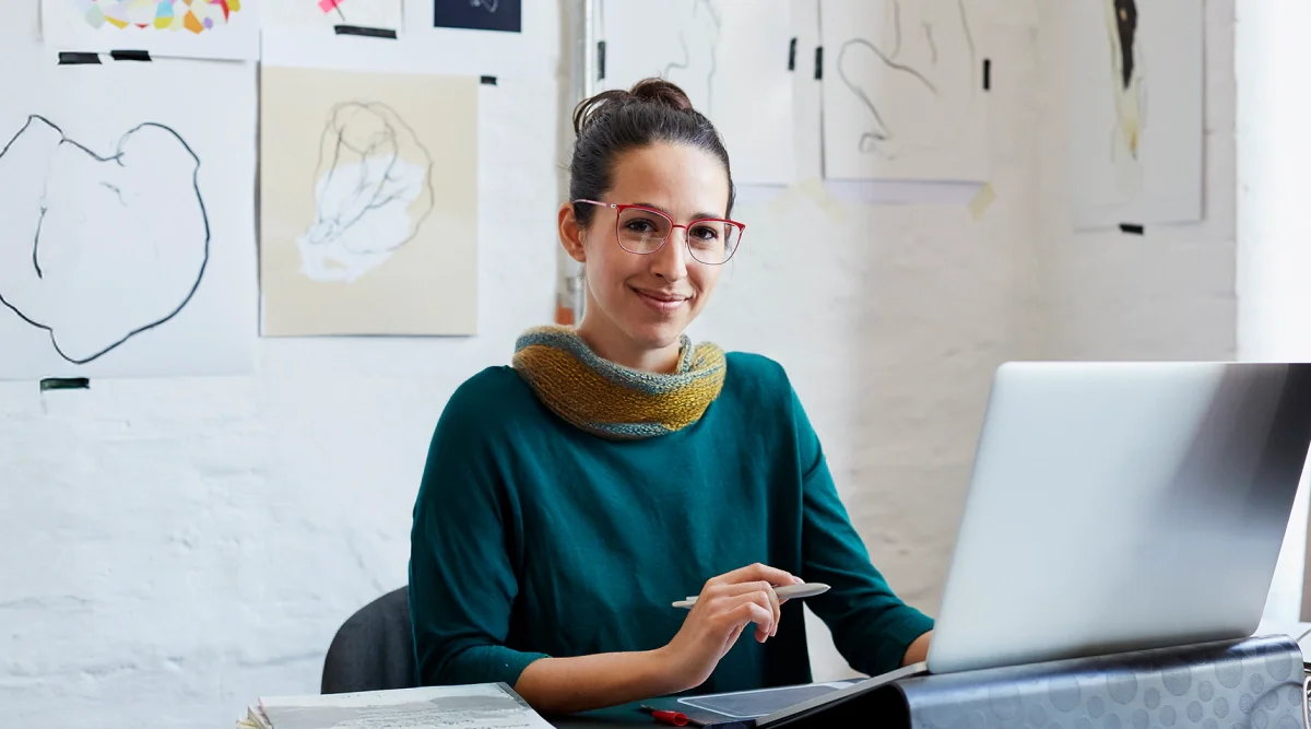 Woman with laptop in art studio, drawings behind