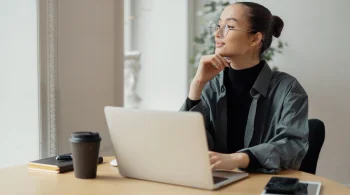 Woman thinking while working on a laptop with a cup nearby