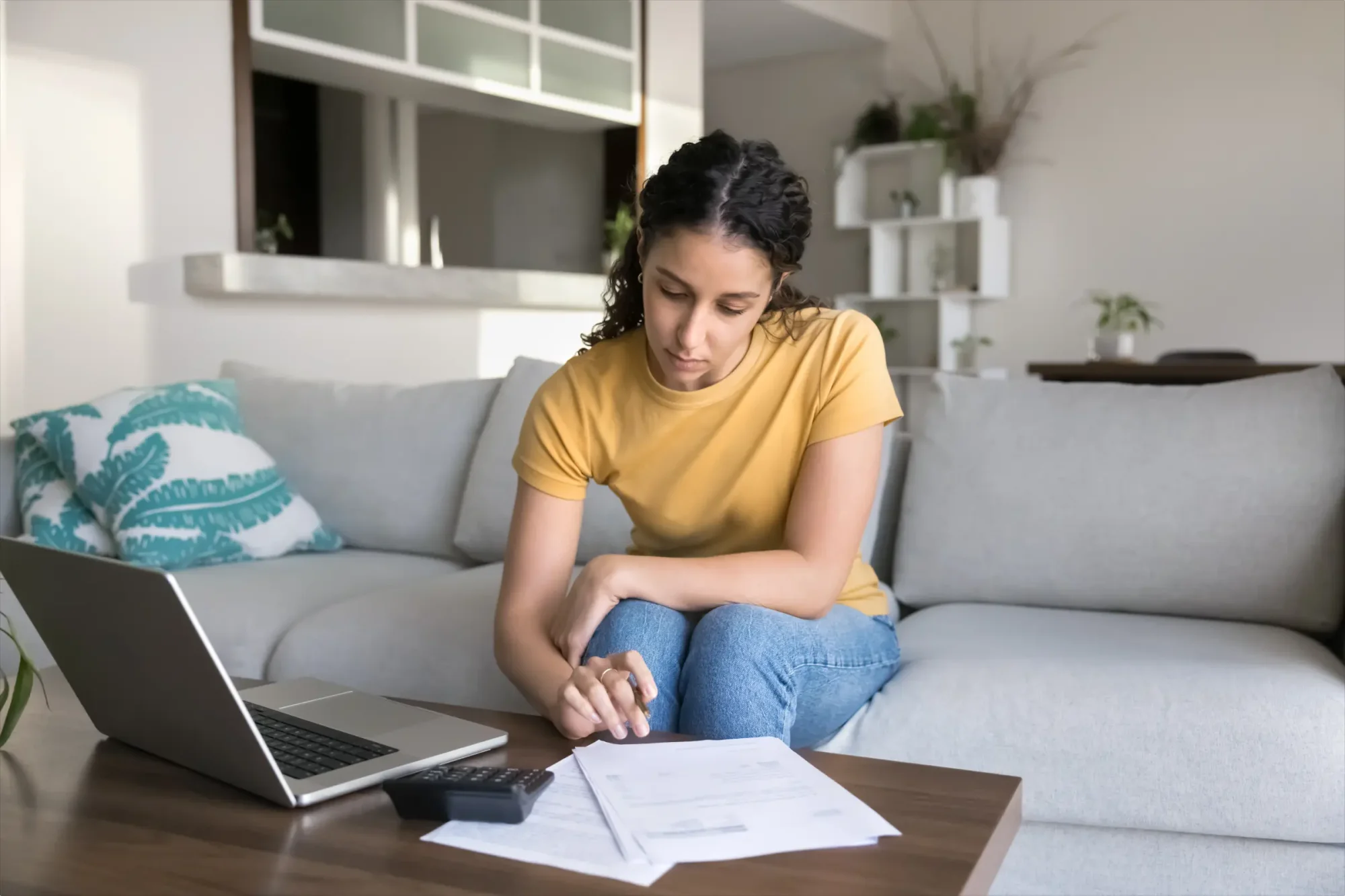 A woman wearing a yellow t-shirt is calculating her taxes for the financial year to avoid unexpected circumstances such as drawing extra estate taxes or incurring fines due to certain late tax submissions.