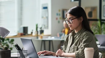 Woman in glasses working on a laptop in a bright office