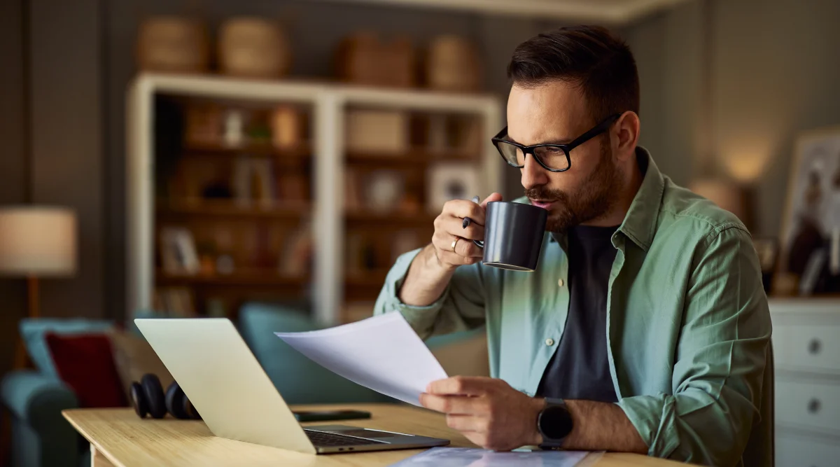 Man holds cup of coffee and looks at computer, thinking about scheduling a K-1 Tax form.