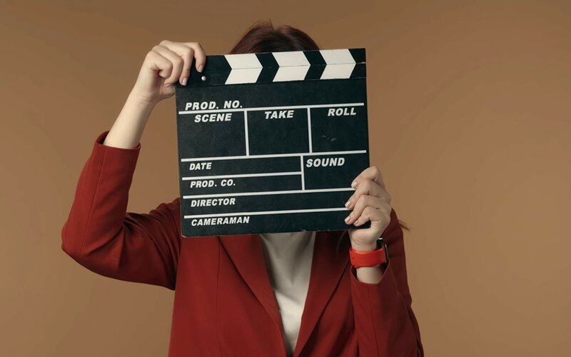 An image of a woman dressed in red, holding a film flap against her face.
