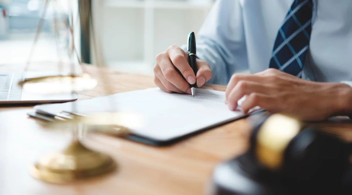 Close-up of a person signing papers at a desk with a tie