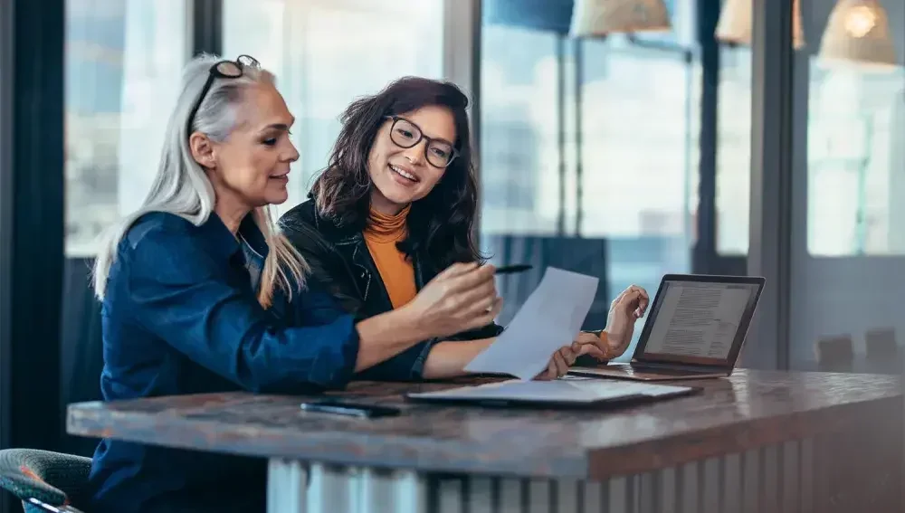 Two owners of a small business sit at a counter and check their Form SS-4 to apply for an EIN.