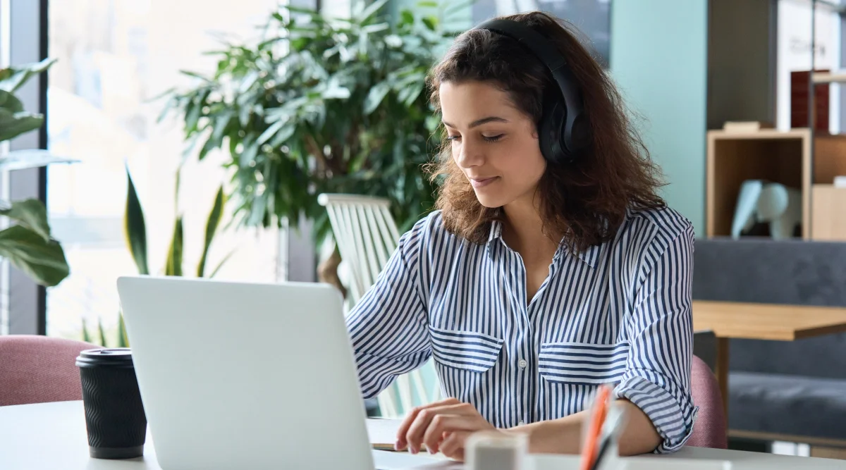 A woman wearing headphones working on a laptop.