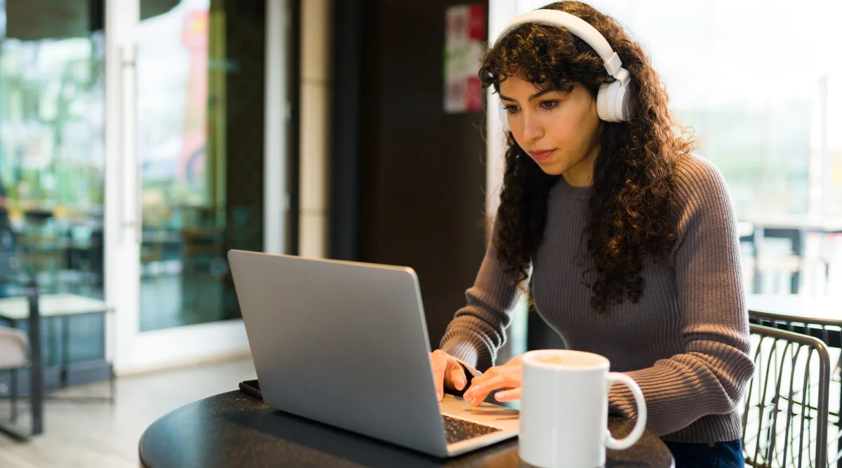 Woman in headphones focused on laptop at a cafe