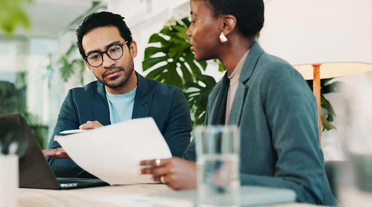 Two people discussing documents at a table with a laptop