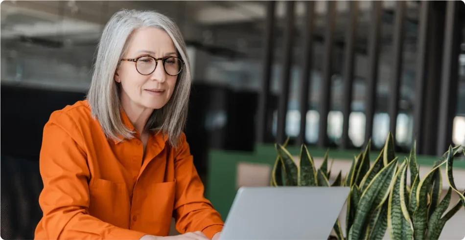 Older White woman with grey hair wearing glasses and a long sleeved orange shirt working on her LegalZoom corporate dissolution on her laptop.