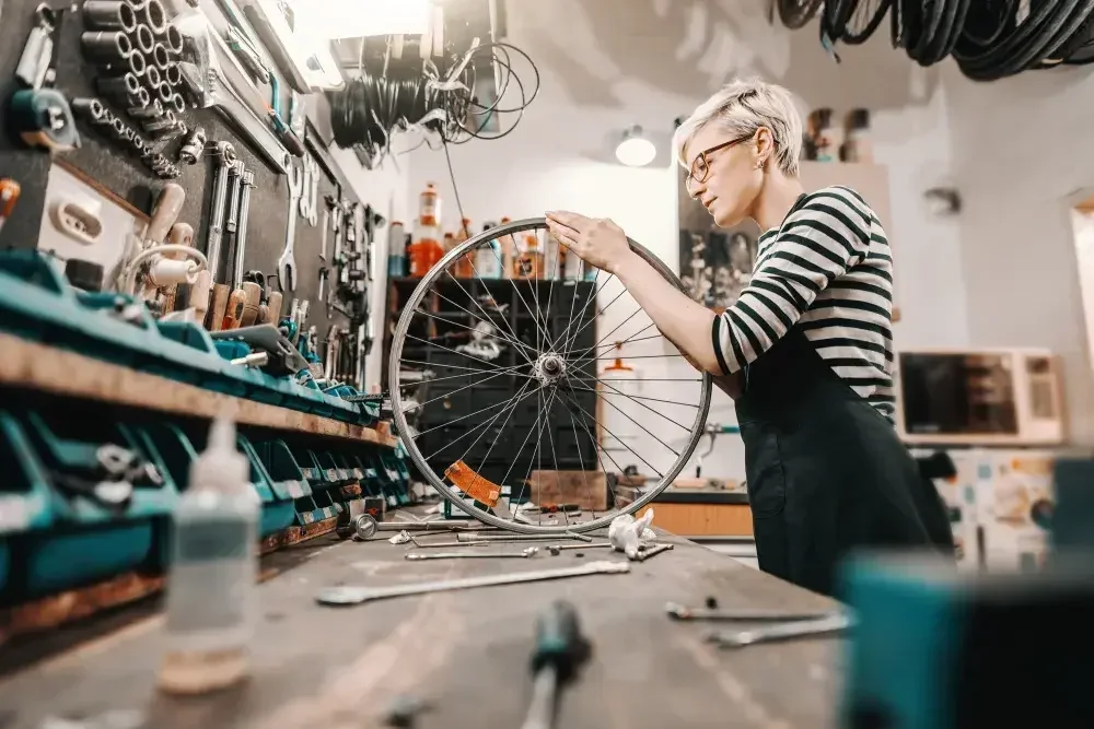 A woman wearing overalls repairs a bike tire in her shop.