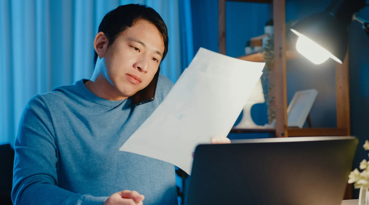 A man talking on the phone while looking at a paper.