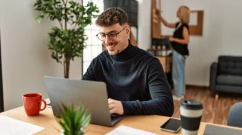 Man happily working on a laptop in a home office with plants