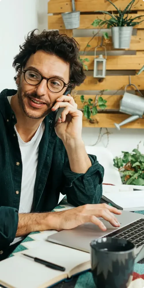 A man sitting at a desk in front of a laptop and consulting an attorney on the phone about creating an independent contractor agreement