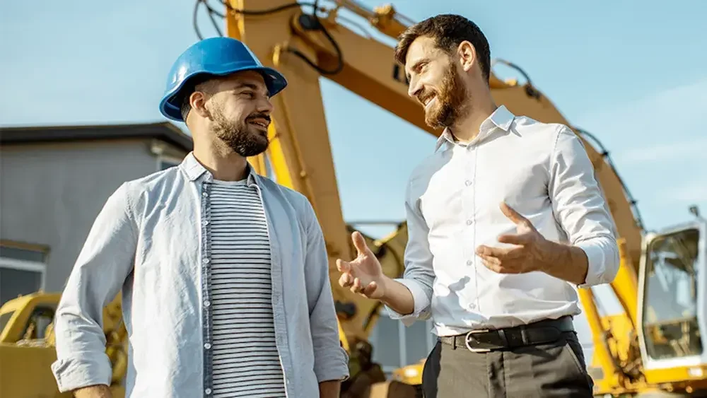 Two men stand in a construction zone talking.
