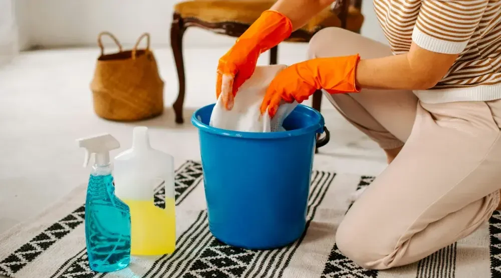 Close-up of a person kneeling at a soapy bucket while wearing gloves.