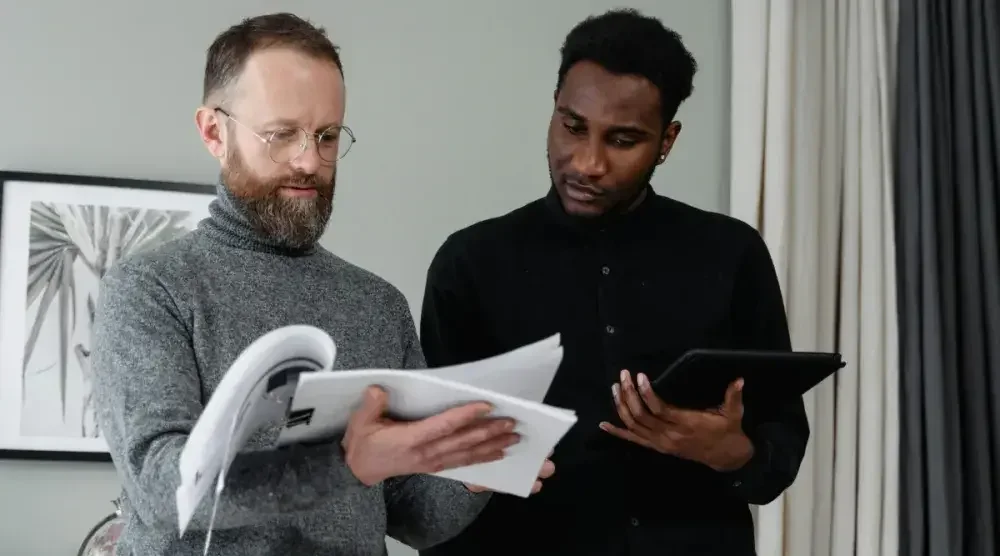 Two men who co-own a business go over their BOIR filing paperwork. One of them holds a report, while the other holds a tablet.