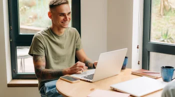 Smiling man using a laptop by the window