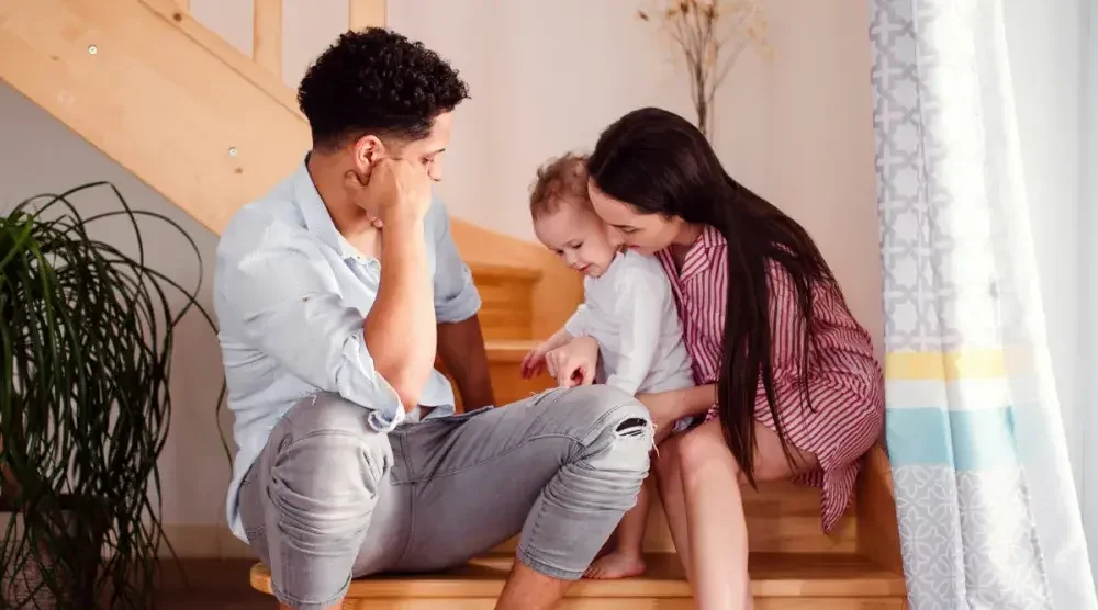 Father and mother sit with their toddler playing on the stairs