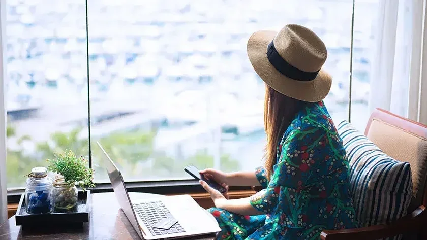 A woman is looking out the window, holding her phone. 