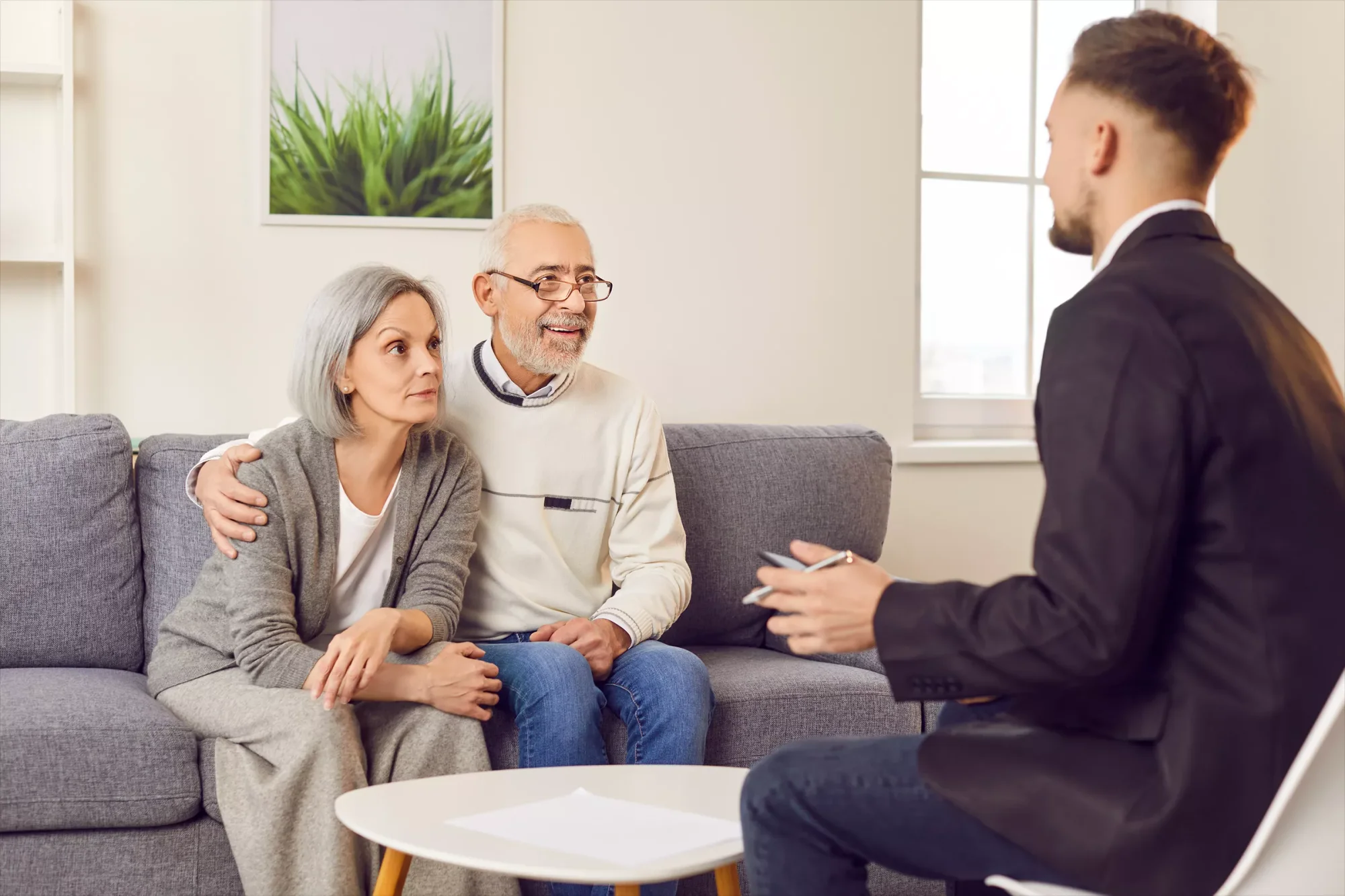 An older couple is sitting on a sofa and talking to an attorney about the importance of selecting the right trustee.