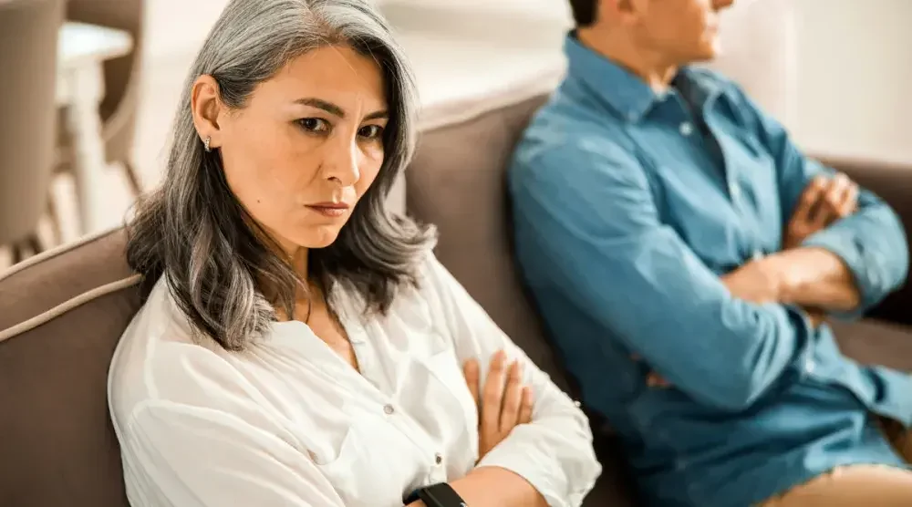 A man and woman sit on a couch with arms folded looking quite upset